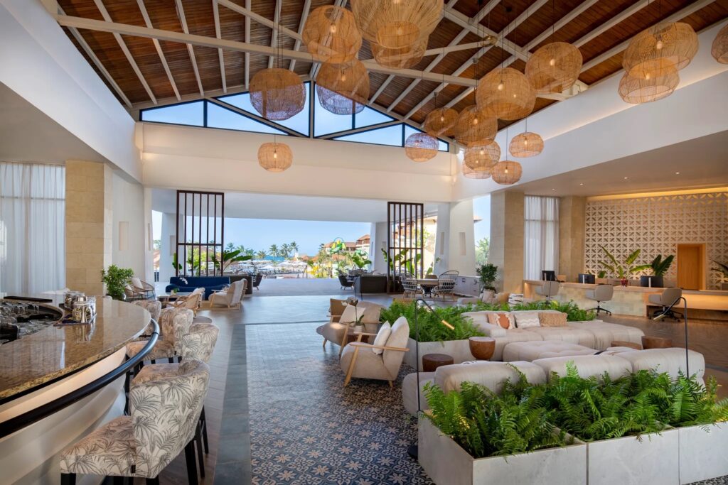 the lobby of a resort overlooking palm trees and with a peaked wooden roof and rafters