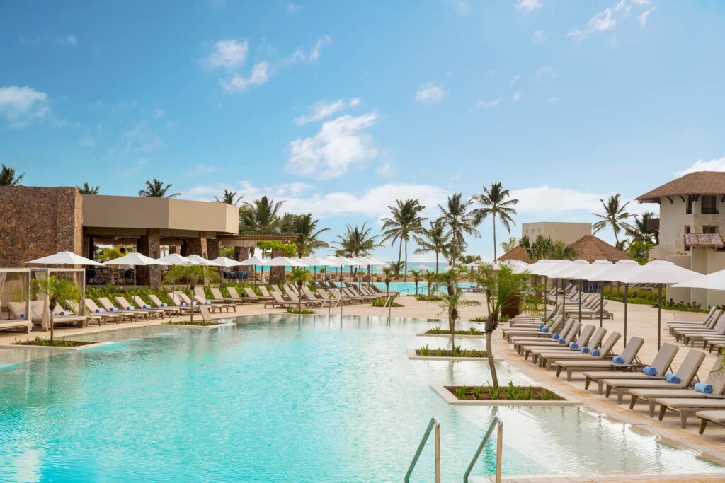 A long narrow pool with rows of lounge chairs on bothsides and umbrella tables behind them