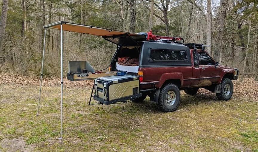 a red pickup with a camper on back and rear awning set up for camping