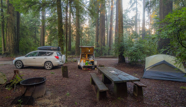 tall trees in background of a tent campsite with a picnic table and white car