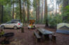 tall trees in background of a tent campsite with a picnic table and white car