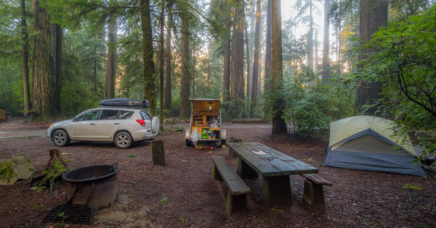 tall trees in background of a tent campsite with a picnic table and white car