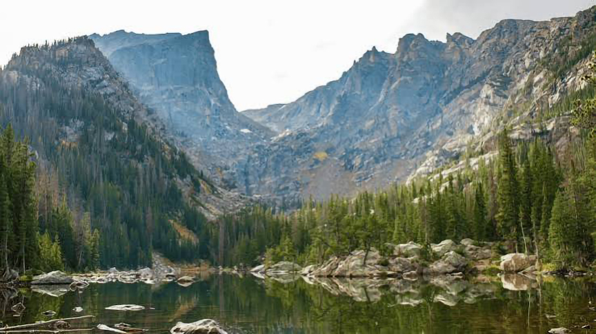 grey rocky mountains in background with greenery and a lake in front of mountains
