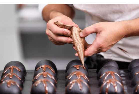 Professional confectioner making chocolate sweets at confectionery shop .